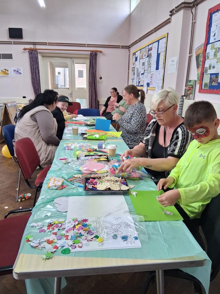 A group of parents and children are doing arts and crafts activities at a long table