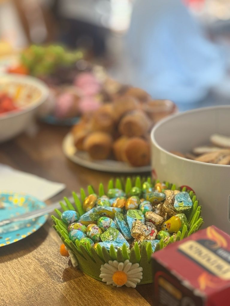 An Easter basket of mini chocolate eggs. Sausage rolls and other party food in the background.