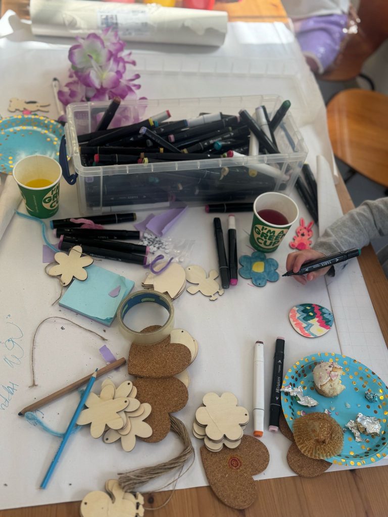 an overhead view of arts and crafts materials on a table. There are cut out flower and heart shapes, sellotape, string, pens and pencils.