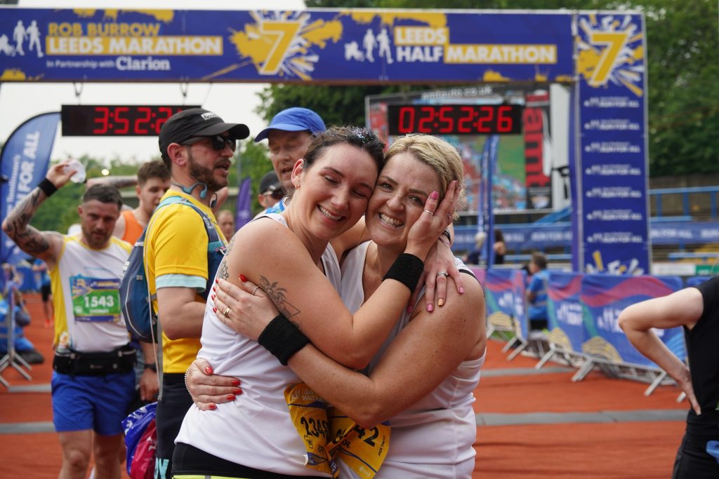 Two women runners embracing and smiling at the finish line of the Leeds Marathon/half marathon