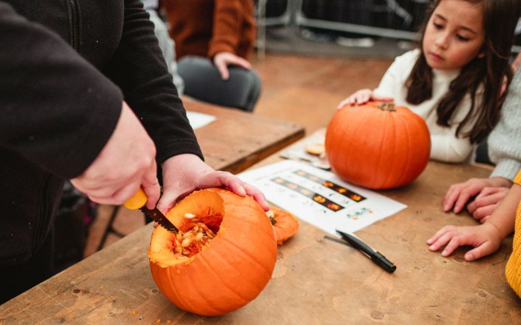 Photo of someone carving a pumpkin with children watching